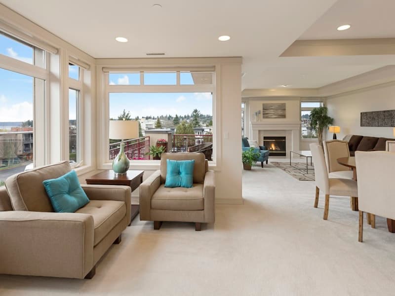 A bright, professionally furnished rental property living area with large windows overlooking a neighbourhood.